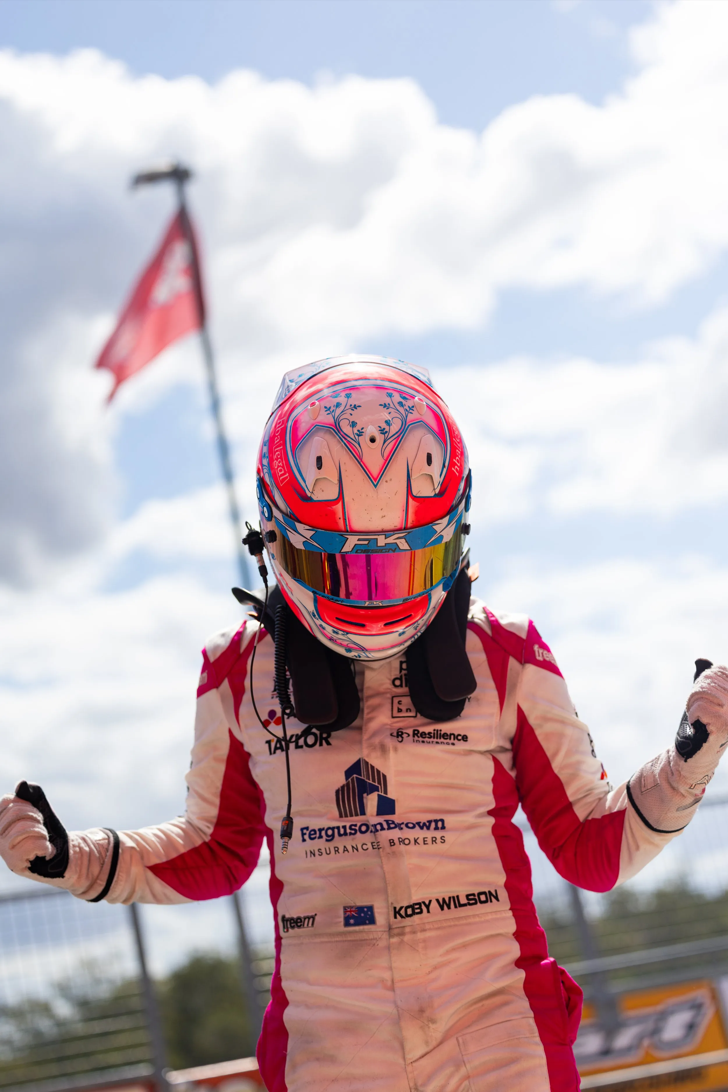 Koby clenching both fists in celebration in his helmet, a red flag flying overhead